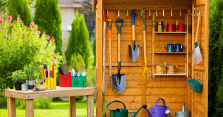 Des outils de jardin suspendus à un râtelier mural en bois.