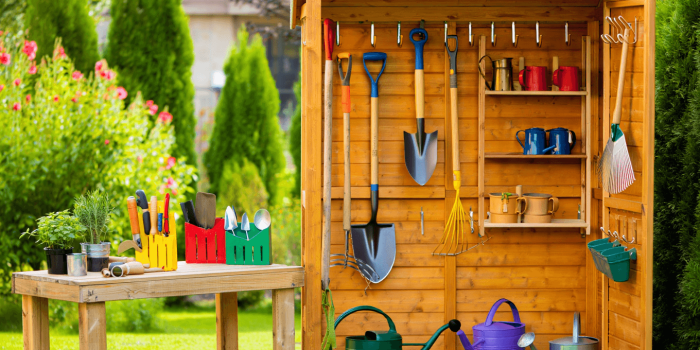 Des outils de jardin suspendus à un râtelier mural en bois.