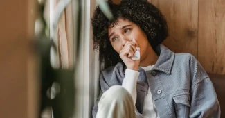 Personne assise seule, regardant par une fenêtre, dans un moment de recueillement et de réflexion sur le deuil.