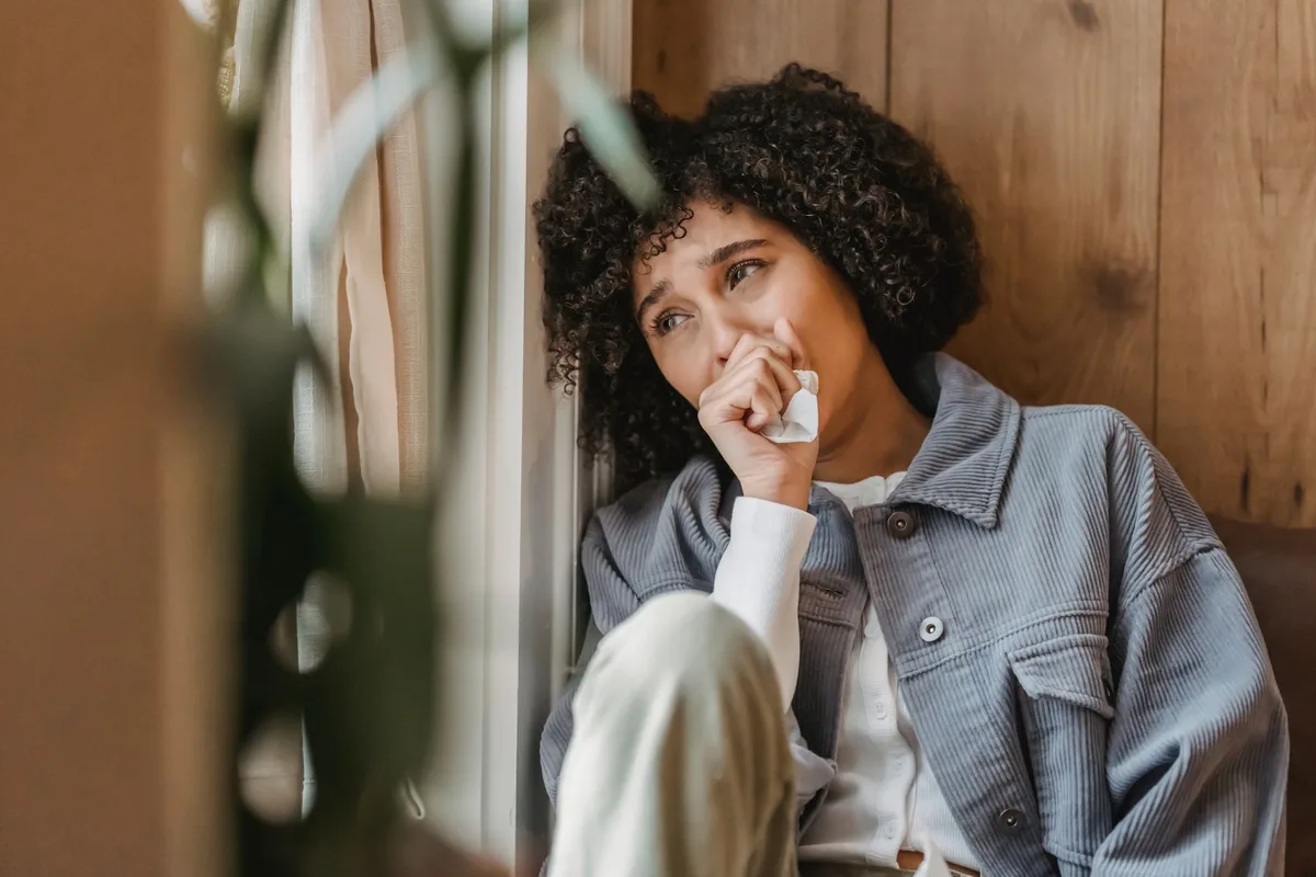 Personne assise seule, regardant par une fenêtre, dans un moment de recueillement et de réflexion sur le deuil.