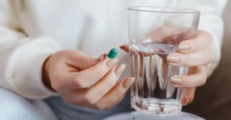 Mains tenant un comprimé de médicament et un verre d'eau sur un bureau