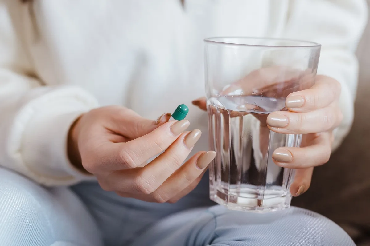 Mains tenant un comprimé de médicament et un verre d'eau sur un bureau