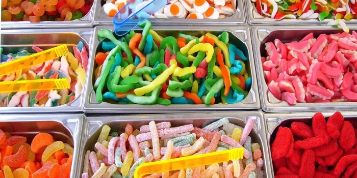 Pot de gummies colorés sur un plan de travail de cuisine, mains prenant un gummy