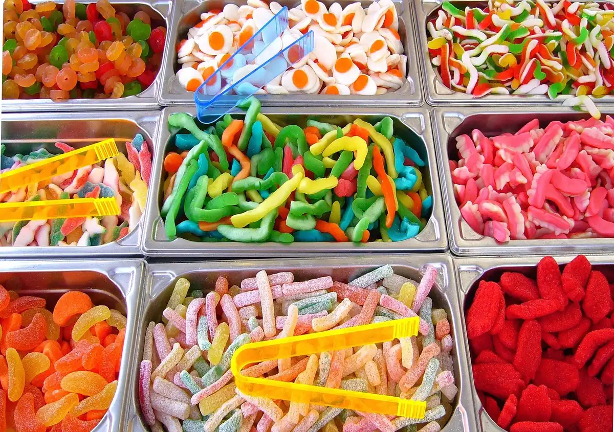 Pot de gummies colorés sur un plan de travail de cuisine, mains prenant un gummy